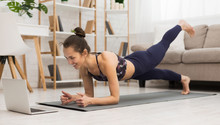 Fit Woman Doing Yoga Plank And Watching Online Tutorials On Laptop
