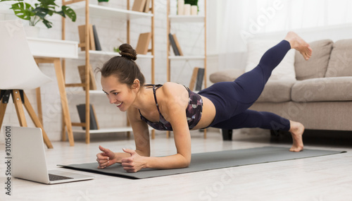 Fotografía Fit woman doing yoga plank and watching online tutorials on laptop