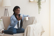 Cheerful black woman using smartphone and drinking coffee on couch