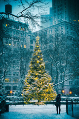 Snow-covered Christmas tree with golden lights glowing against a stark urban background after a winter blizzard in New York City