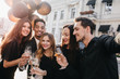 © Look! - Blissful african man holding bunch of balloons and glass of wine in front of old building. Outdoor portrait of excited friends enjoying champagne during meeting after workday.