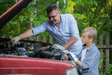 Young father teaching his son to change motor oil in family car.