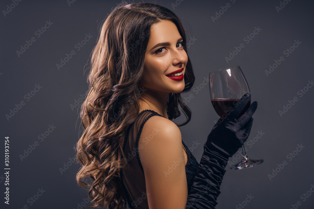 Photo Stock Glamour caucasian brunette woman in evening black dress on a  neutral background. She pose sensually with glass of wine. Retro fashion  mood. | Adobe Stock