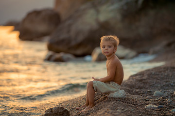 Little boy in shorts during sunset on sea stone.