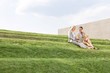 © MDBPIXS - Young businesswomen using laptop together while sitting on grass steps against sky