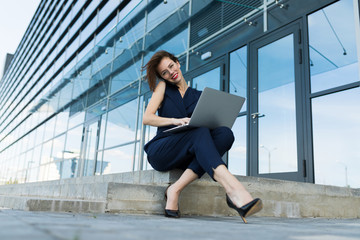 Caucasian woman in office clothes do freelance with laptop and waits colleague near the office building