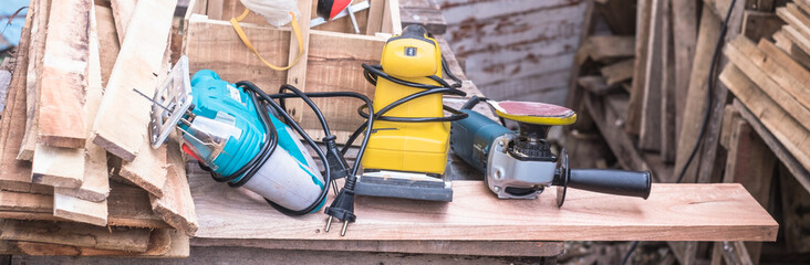 Woodworking power tools including rectangular orbit sander, grinder and jig saw with wooden tool box at outdoor workshop.