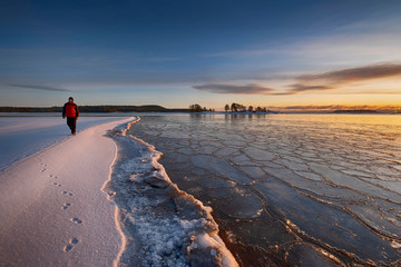 man tourist goes along  first ice  off the coast on the water in Lake Ladoga at dawn with fresh snow in winter