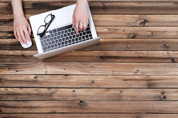Poster - Female hands typing on laptop keyboard and using mouse on wooden table
