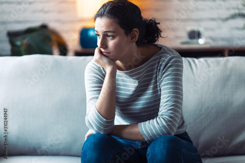 Fotografía Boring young woman looking to side and thinking while sitting on the sofa at home