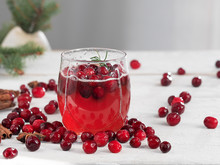 Fresh Cranberry Drink In A Glass Cup On A Wooden White Background. Close-up. Horizontal Orientation. Cranberries And Spices On The Table.