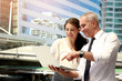 © Stella - Senior businessman and young businesswoman using laptop together, discussing about work outdoor office at oudowntown city, happy smiley people talking  their job. Boss and secretary meeting outside of