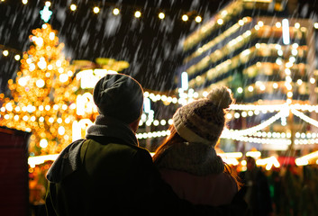 The couple are looking at the decorated Christmas market in the evening