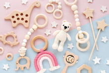 Cute Wooden Baby Toys On Pink And Light-blue Background. Knitted Bear, Rainbow, Dinosaur Toy, Beads And Stars. Eco Accessories,  Beanbag And Teethers For Newborn. Flat Lay, Top View