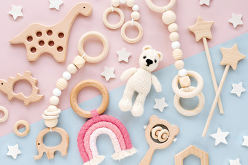 cute wooden baby toys on pink and light-blue background. knitted bear, rainbow, dinosaur toy, beads 