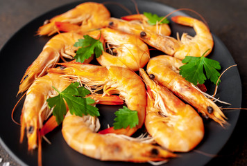 raw prawns waiting for the cook to grill, in a black plate with herbs and spices on a stone background 