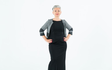 Mature middle aged woman with gray hair in a black dress on a light background.