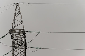 Cables and modular suspension insulators for overhead power line. Transmission tower. Metal construction. The sky in the fog, gray gloomy day. Industry as a cause of environmental pollution.