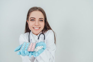 Closeup portrait of young female intern showing her palms full of different pills, looking at the camera, smiling pleasantly.