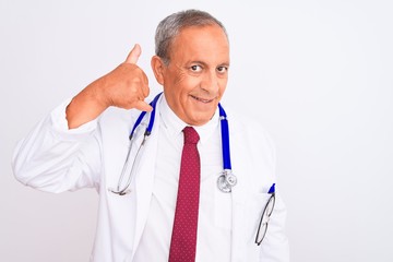 Sticker - Senior grey-haired doctor man wearing stethoscope standing over isolated white background smiling doing phone gesture with hand and fingers like talking on the telephone. Communicating concepts.