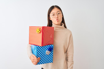 Sticker - Young chinese woman holding birthday gifts over isolated white background making fish face with lips, crazy and comical gesture. Funny expression.