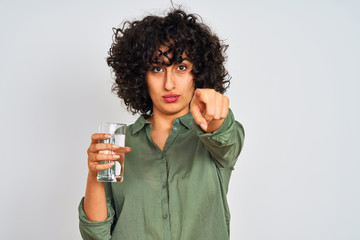 Sticker - Young arab woman with curly hair holding glass of water over isolated white background pointing with finger to the camera and to you, hand sign, positive and confident gesture from the front