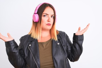 Sticker - Young beautiful woman listening to music using headphones over isolated white background clueless and confused expression with arms and hands raised. Doubt concept.