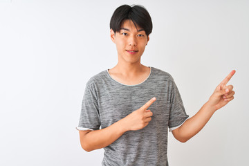 Poster - Young chinese man wearing casual t-shirt standing over isolated white background smiling and looking at the camera pointing with two hands and fingers to the side.