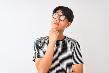 Wall Mural - Chinese man wearing glasses and navy striped t-shirt standing over isolated white background with hand on chin thinking about question, pensive expression. Smiling with thoughtful face. Doubt concept.