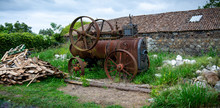 Rusty Antique Farm Equipment Next To Stone Building