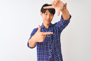 Wall Mural - Young chinese man wearing casual blue shirt standing over isolated white background smiling making frame with hands and fingers with happy face. Creativity and photography concept.