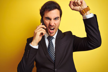 Poster - Young handsome businessman talking on the smartphone over isolated yellow background annoyed and frustrated shouting with anger, crazy and yelling with raised hand, anger concept