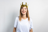Fototapeta Panele - Young woman with a crown on her head emotionally rejoices and celebrates on a light background. Emotion laughter, surprise, shock. Concept of a queen, luck, victory, dream, goal, aspiration. Banner