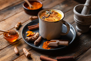 Golden milk in white mug, turmeric latte made with curcuma, cinnamon, anise, honey. Healthy hot winter drink, natural, organic beverage. Close up, front view.  Wooden rustic background