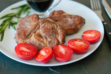 Wall Mural - Fragrant pork meat steaks with spices, tomatoes and sauce, on a gray plate, on a dark concrete background, close-up