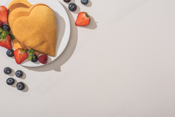 Wall Mural - top view of heart shaped pancakes with tasty berries on plate on white background