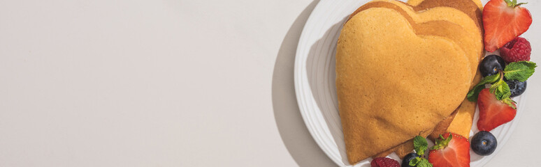 Wall Mural - top view of heart shaped pancakes with tasty berries on plate on white background, panoramic shot