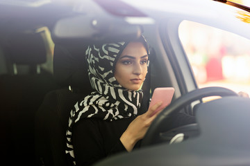 Wall Mural - muslim girl driving car and texting on her smart phone