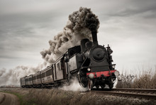 Vintage Steam Train With Ancient Locomotive And Old Carriages Runs On The Tracks In The Countryside