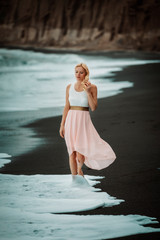 Wall Mural - blond woman on a black beach on Santorini, with cliff in the background and a rough sea