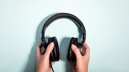 Black massive headphones in female hand on pastel background, copy space. Modern technology flat lay with over-ear earphones in woman hand, modern lifestyle concept