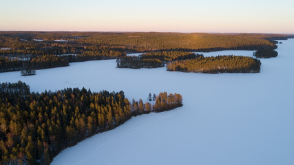 Wall Mural - Aerial view of a gold sunset over winter snow-covered forest.  Aerial drone view of a winter landscape.  Beautiful sunset sky over frozen lake.