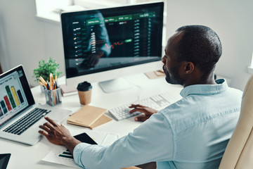 Rear top view of young African man in shirt using computer while working in the office