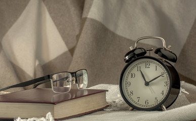 Vintage alarm clock, book and glasses on a background of a checkered plaid.