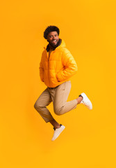 Wall Mural - Joyful afro guy in warm jacket jumping in the air