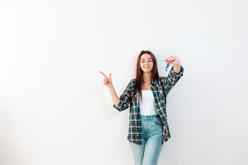 Buying and renting real estate. A smiling woman in jeans and a shirt holds a bunch of keys and points with her free hand to the left. White background and copy space