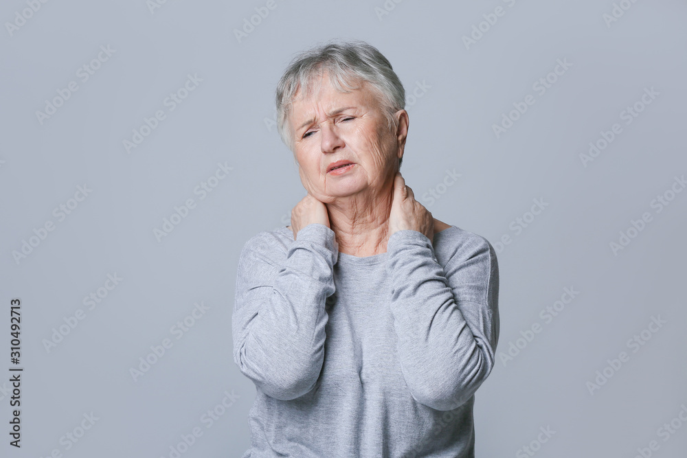 Senior woman suffering from neck pain on grey background