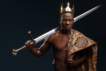 African man in a crown and cloak holds a sword in his hand.