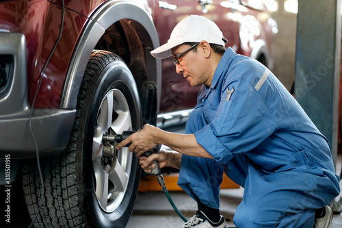 Fotomural Asian automotive mechanic with white cap and blue uniform is working with replace or fix the problem of car wheel in the garage