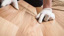 Installing Laminated Floor, Detail On Man Hands In White Gloves Fitting Wooden Tiles